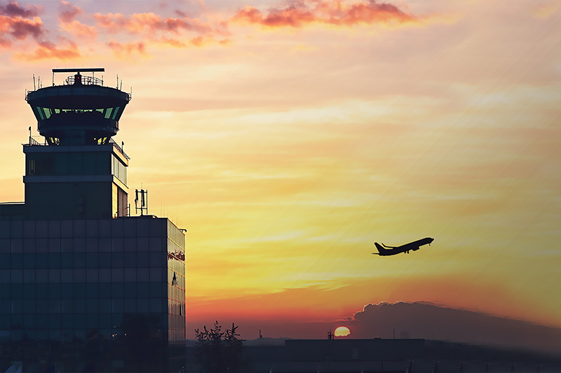 An air traffic control tower with an airliner taking off in the distance