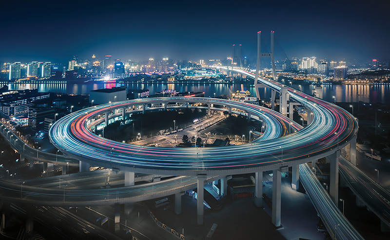 A circular highway ramp by a city with cars speeding along