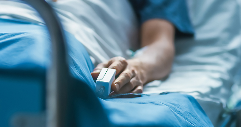 Patient in hospital bed with blood oxygen sensor on finger