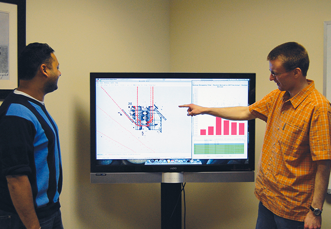 Two analysts view ground traffic patterns on a large monitor