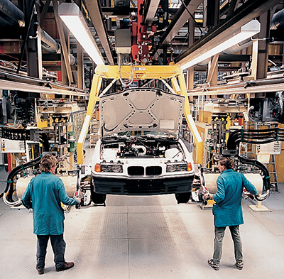 Two workers with a car hoisted up in an automotive factory