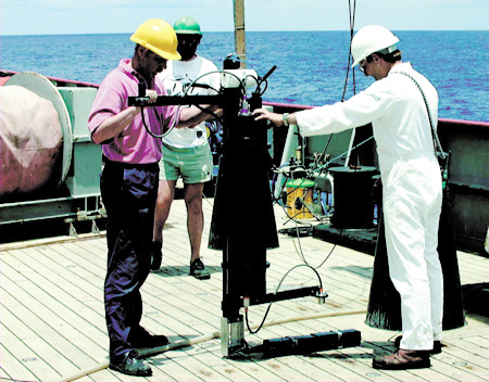 SeaSpec spectroradiometer on the deck of a ship with two men holding onto it and another man standing in background