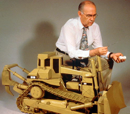 A researcher kneels down next to a 1/8 scale replica of the world’s largest earthmover caterpillar tractor