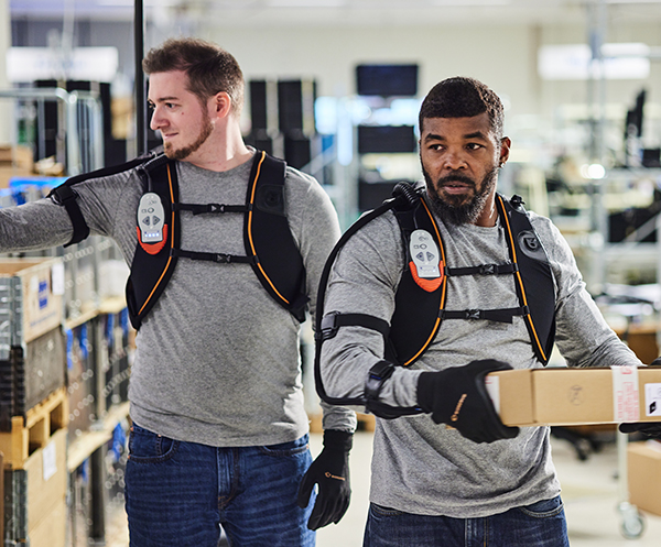 Ironhand being used with its backpack by two warehouse workers