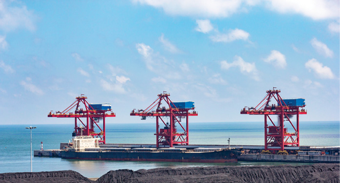 Three red steel structures on water behind black hills of a coal mine