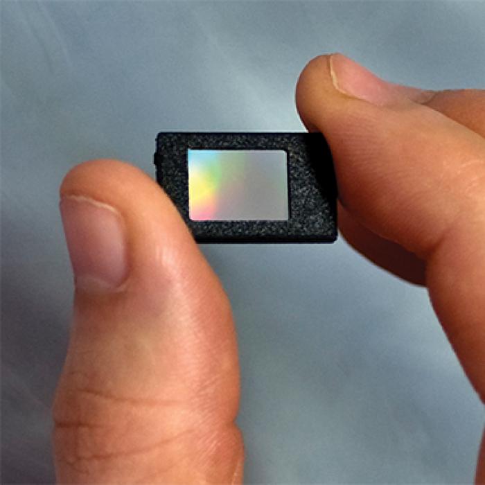 A thumb and forefinger hold a thumbnail-sized microdisplay panel.