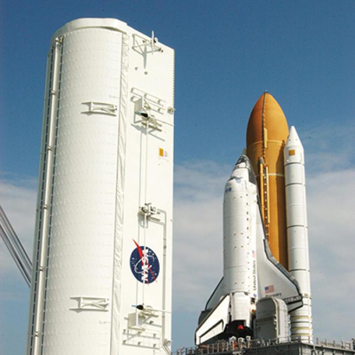 Space Shuttle Discovery on launch pad with large payload canister beside it