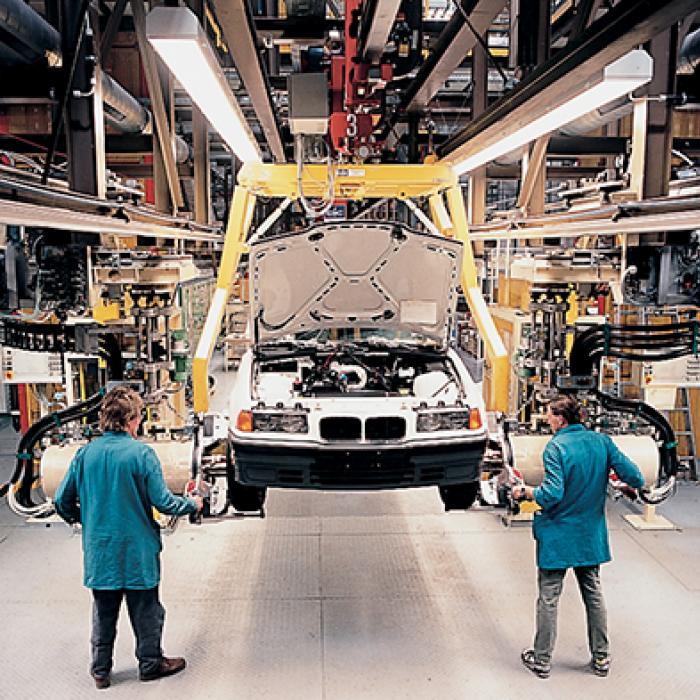 Two workers with a car hoisted up in an automotive factory