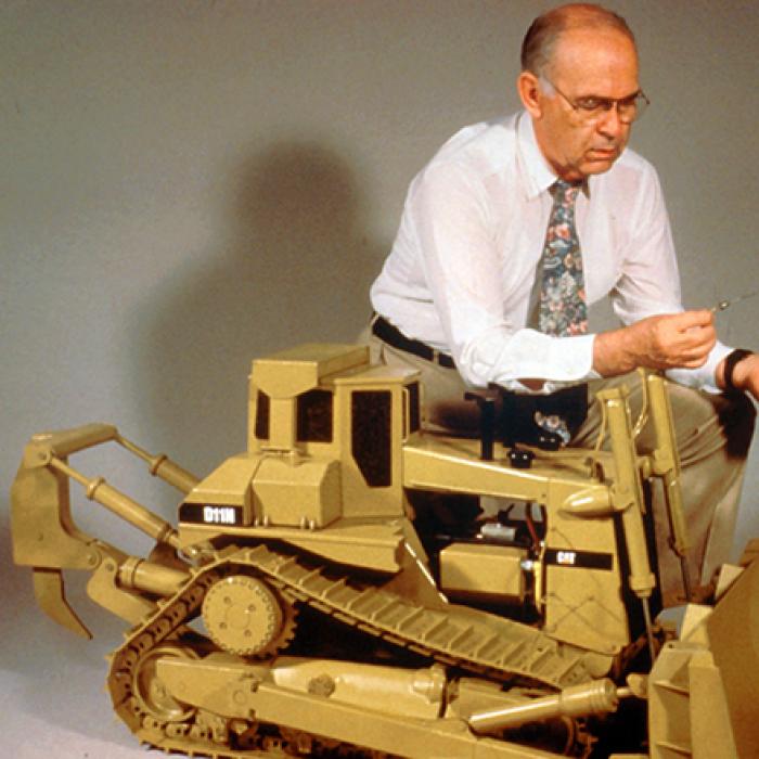 A researcher kneels down next to a 1/8 scale replica of the world’s largest earthmover caterpillar tractor