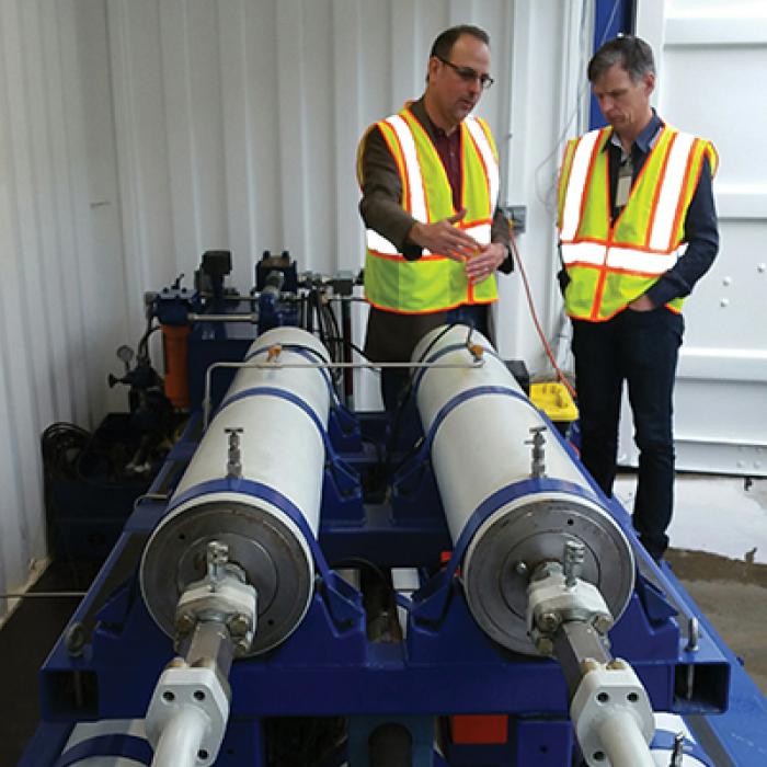 Two men with reflective safety vests standing near SureShear chambers