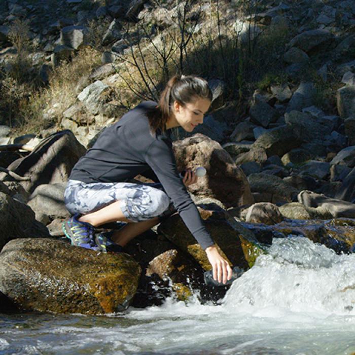 A woman fills a Pod+ water bottle from a flowing stream