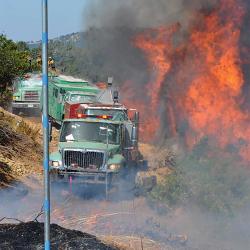 A convoy of firetrucks next to raging forest fire