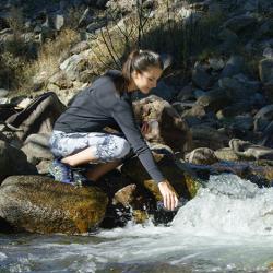 A woman fills a Pod+ water bottle from a flowing stream